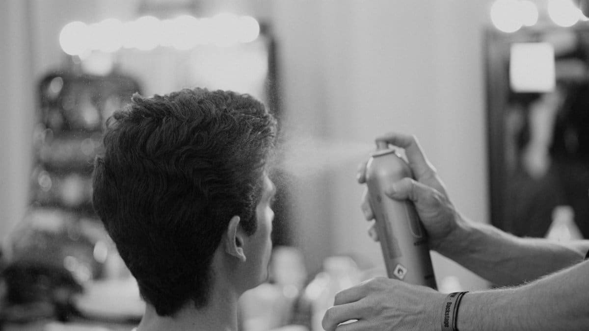 A hairdresser styling a man's hair in a Barcelona salon, using hairspray.