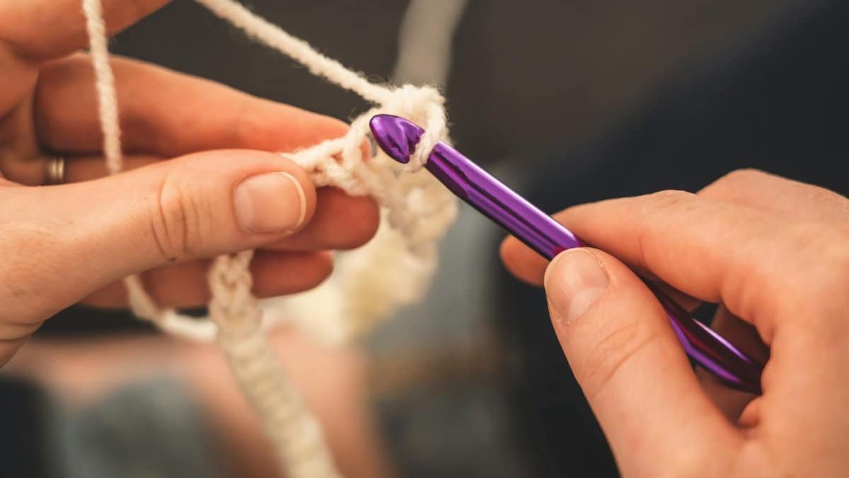 Hands skillfully crocheting with a purple hook and cream yarn, highlighting craftsmanship.