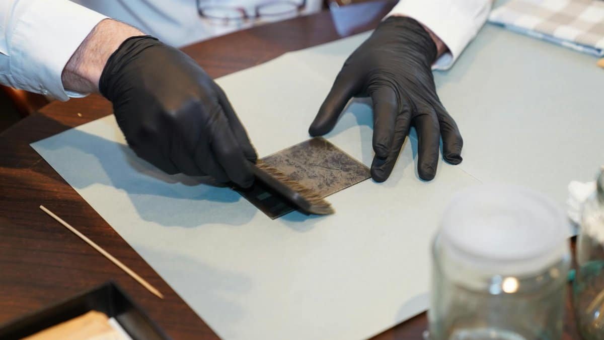 A restorer carefully working on a photograph with gloves and brush, focusing on details.