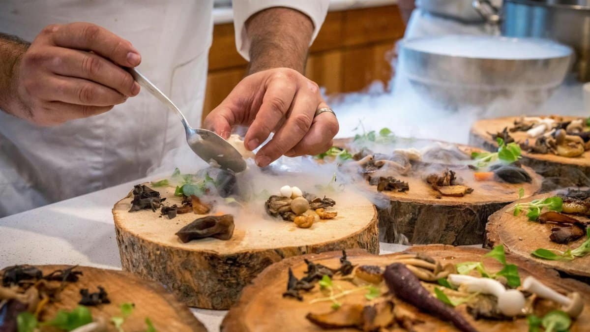 A chef artfully plating a gourmet dish with mushrooms and greens on wood slices.