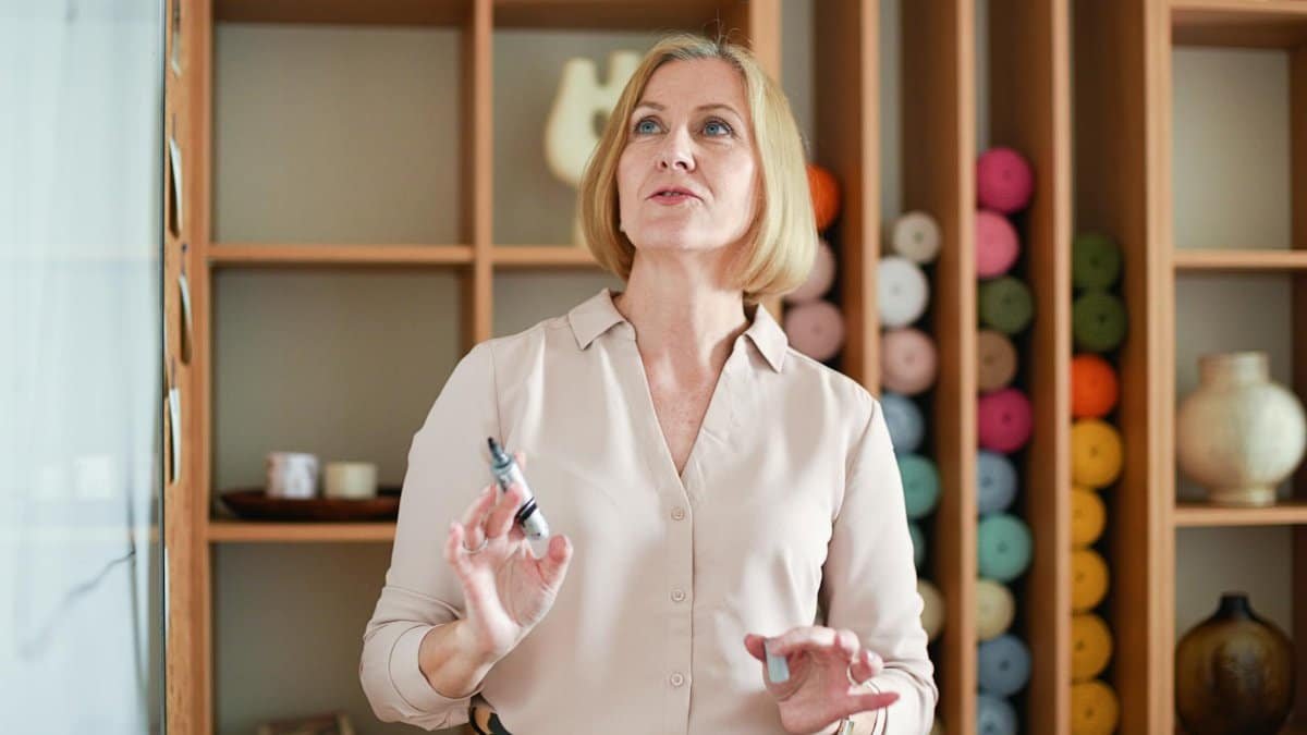 A woman presenting in a cozy studio filled with colorful yarns, using a marker.