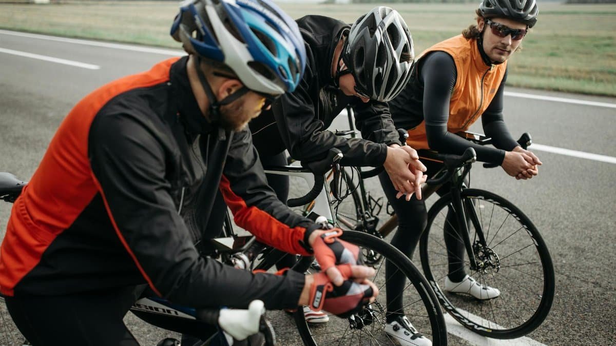 Three cyclists resting on a rural roadside, taking a break from their ride in sporty attire.