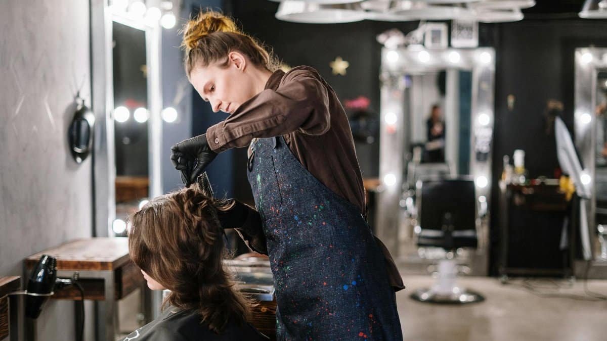 A female stylist expertly applying hair color to a client in a modern salon setting.