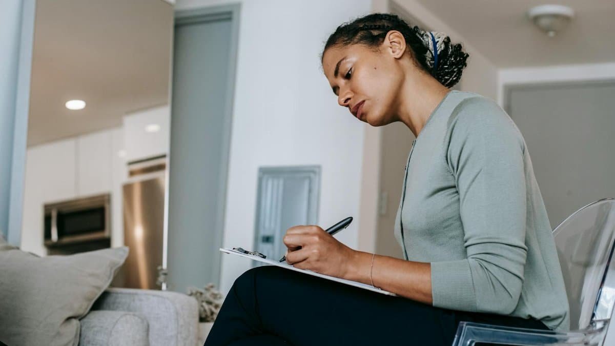 A focused woman writing on a clipboard, possibly a therapist in an office, reflecting professional concentration.
