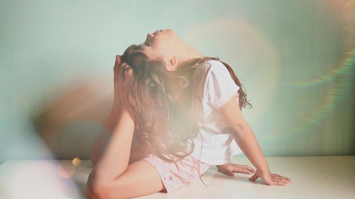 A serene image of a young girl practicing a yoga pose indoors, illuminated by soft sunlight.