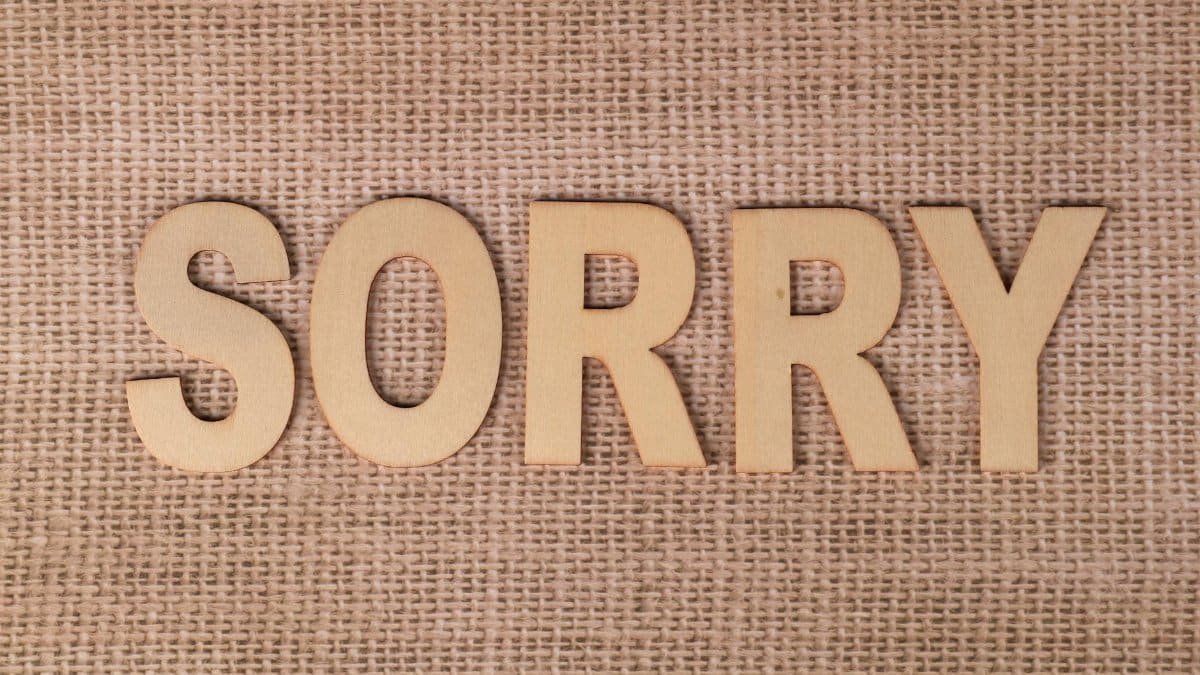 Wooden letters forming the word 'sorry' on a burlap fabric background.