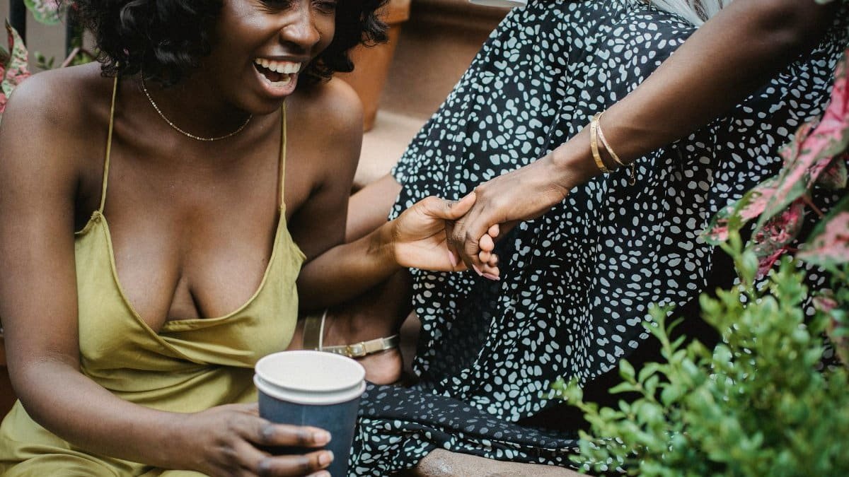 Two women enjoying laughter and coffee outdoors, capturing a candid moment of happiness and friendship.