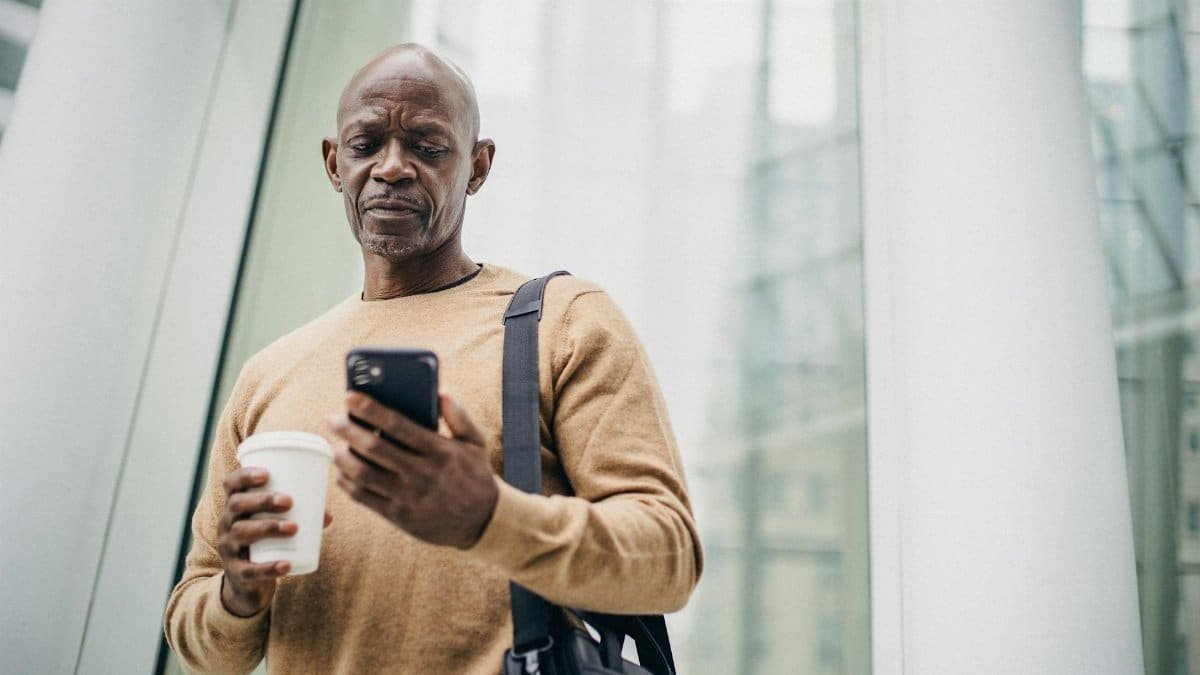 Middle-aged man with coffee checks his smartphone in the city.