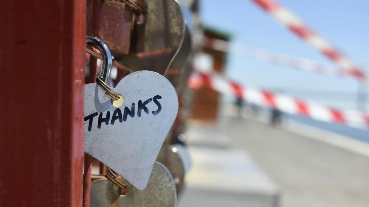 A heart-shaped love lock with 'THANKS' inscribed, hanging on a fence, symbolizing gratitude.