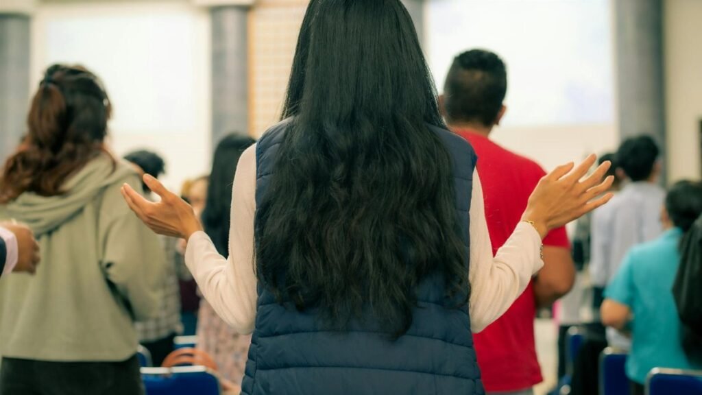 Back view of a diverse group gathered indoors with raised arms, symbolizing unity.