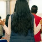 Back view of a diverse group gathered indoors with raised arms, symbolizing unity.