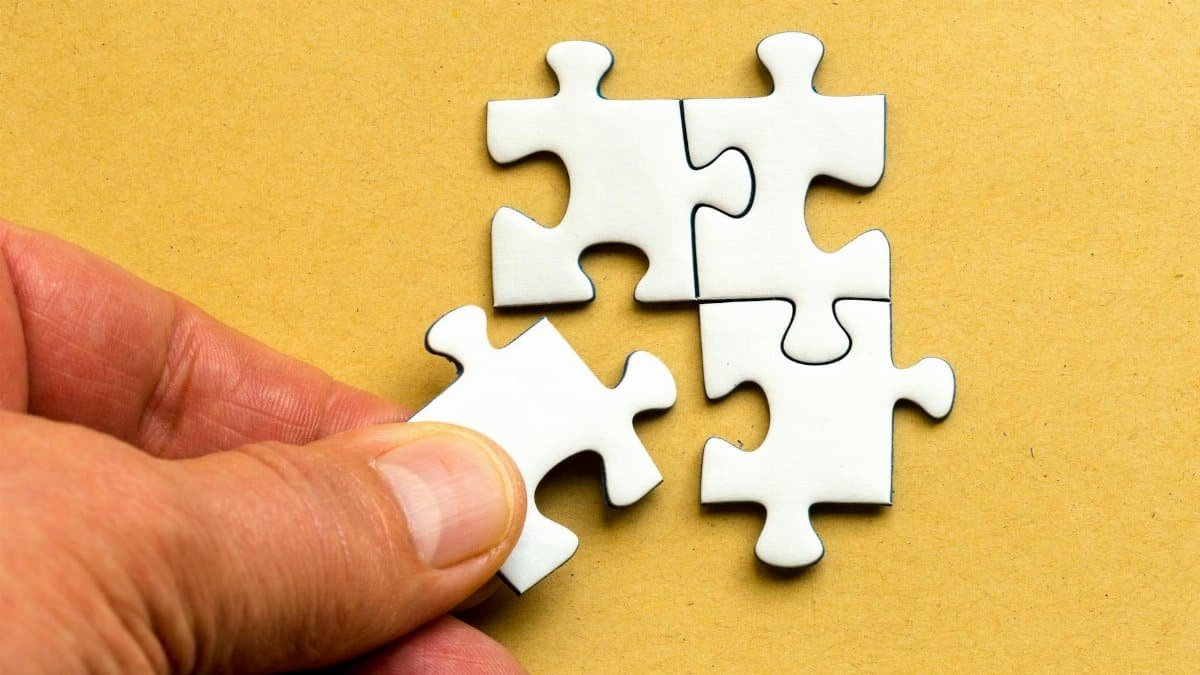 Close-up of a hand completing a white jigsaw puzzle on a yellow background.