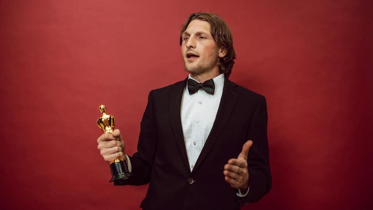An accomplished man in a tuxedo holding a trophy, symbolizing triumph and recognition, against a red backdrop.