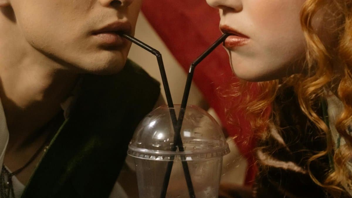 Close-up of a couple sipping from a shared drink with black straws in a plastic cup.