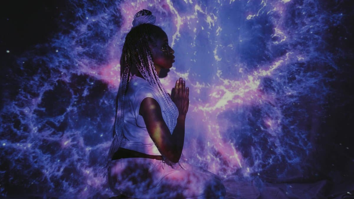 A woman kneels in a galaxy projection, creating a mesmerizing cosmic backdrop.