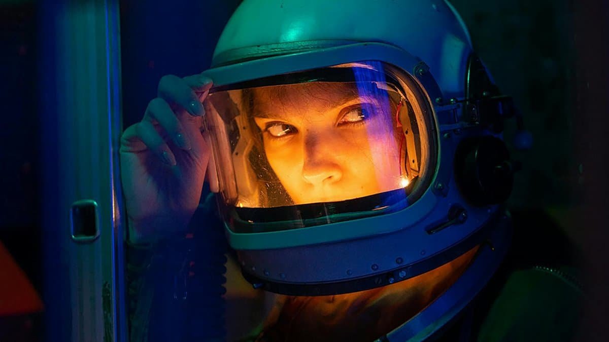 Portrait of a spacewoman in a helmet gazing intensely with colorful lighting.