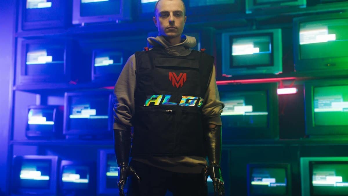 A man stands confidently in front of illuminated screens wearing prosthetic hands. Tech meets humanity.