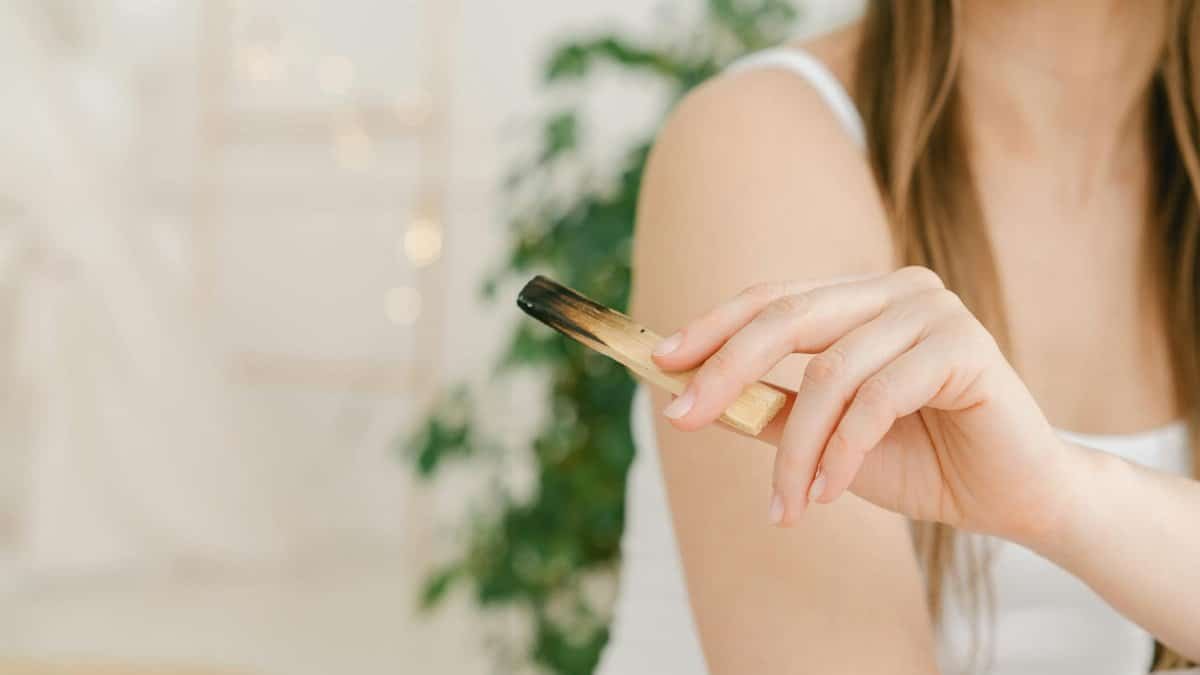 A woman in a calm setting holding a Palo Santo stick, embodying relaxation and mindfulness.