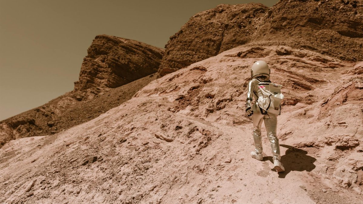 Astronaut in a space suit walking uphill on a rocky, desert-like alien planet.