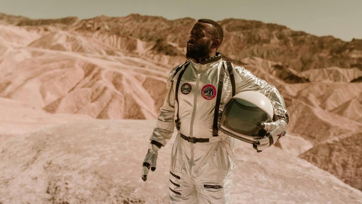 A man in a spacesuit explores a rocky desert, resembling an alien planet's surface.