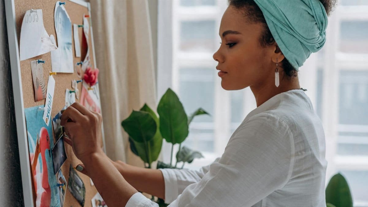 Woman creating a vision board with images in a stylish home setting, showcasing creativity and focus.