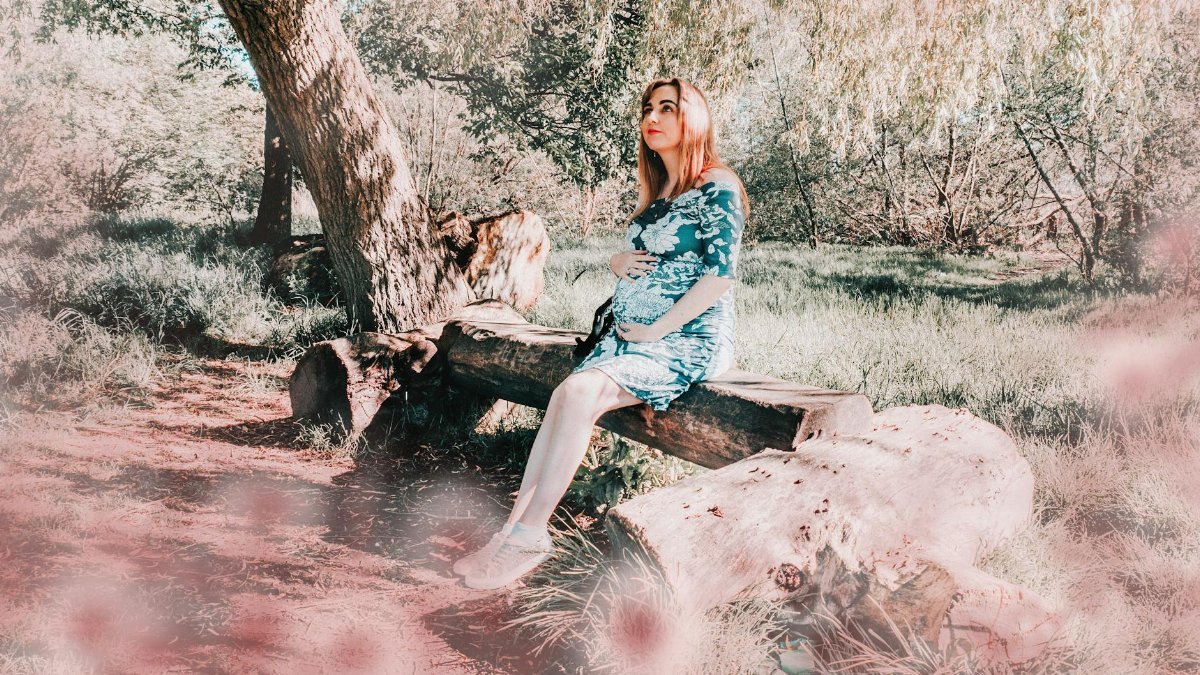 Pregnant woman posing on a log outdoors surrounded by nature.