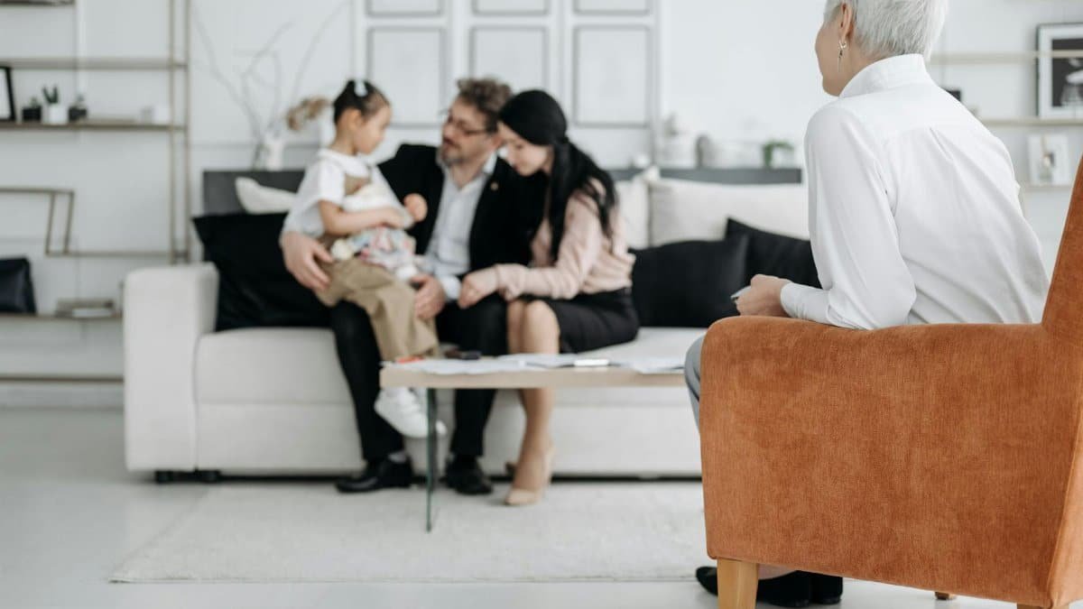 A joyful family adoption meeting with a social worker observing a couple embracing their new child.