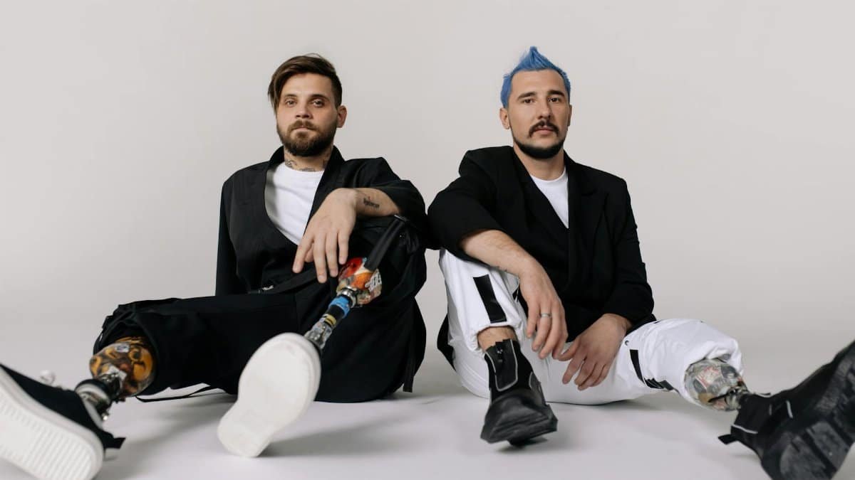 Two stylish men with prosthetic legs sitting in a studio, embodying modern fashion and empowerment.