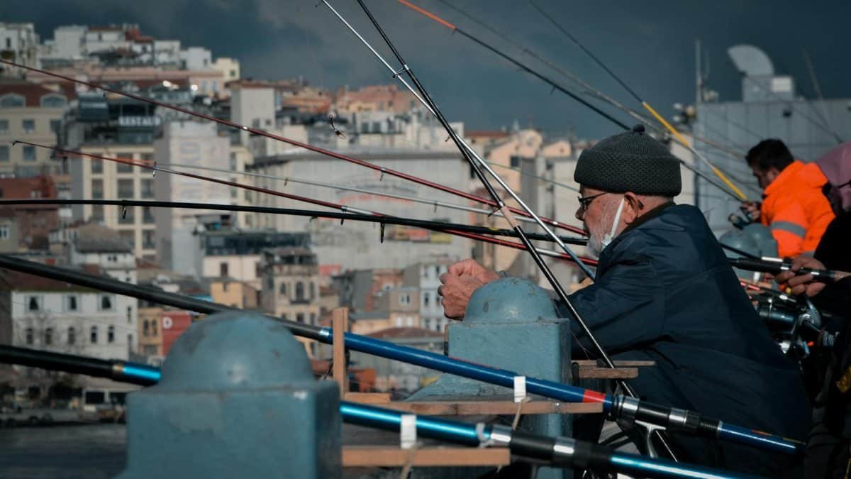 Elderly man enjoying fishing on a bustling city bridge with multiple rods.