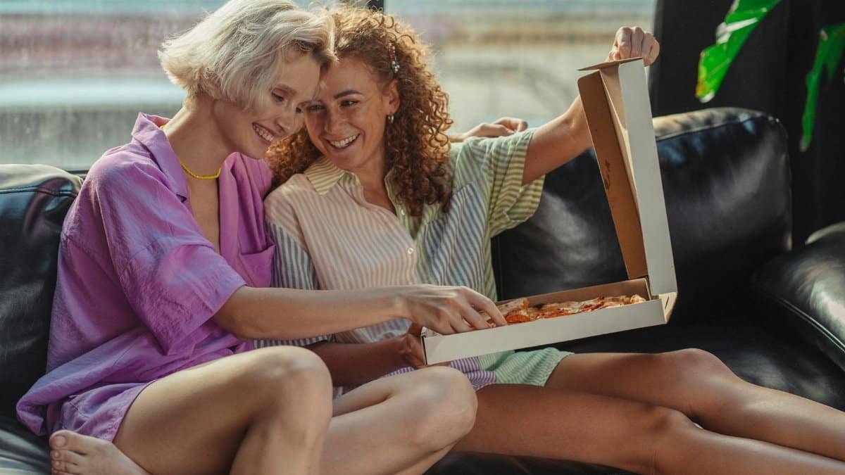 Joyful couple sitting on the couch sharing a pizza, highlighting love and togetherness.