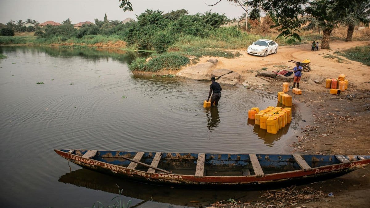 People collecting water containers from a river in a rural setting.
