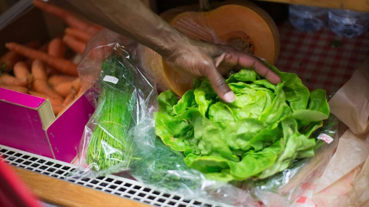 A close-up of a hand picking fresh green lettuce from a grocery shelf with vegetables.