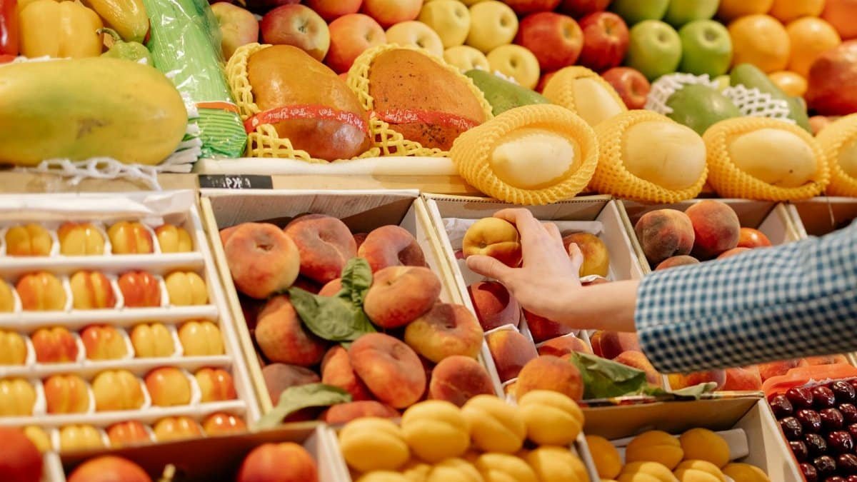 A colorful variety of fresh fruits at a market stand with a hand selecting a peach.