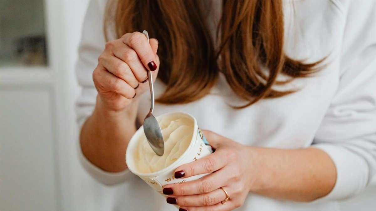 Close-up of a woman scooping delicious vanilla ice cream with a spoon indoors.