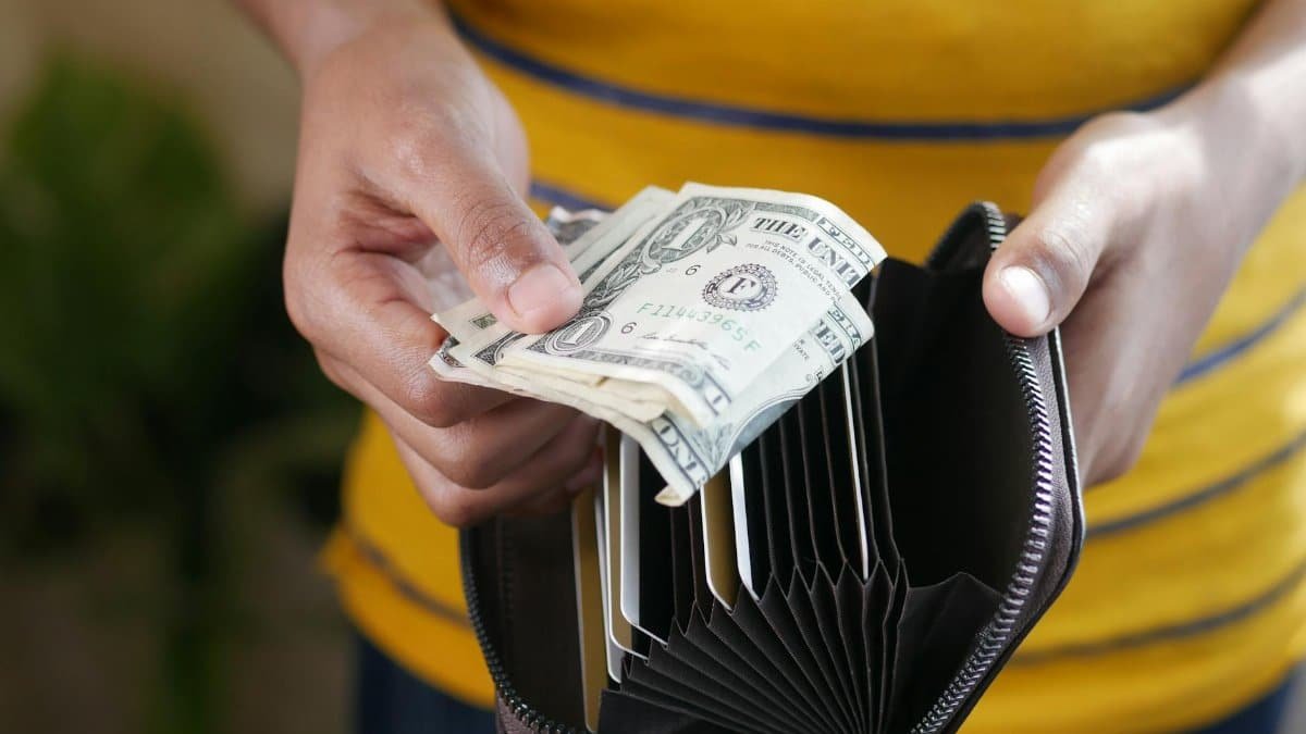 Close-up of a person's hands holding US dollar bills and a wallet.