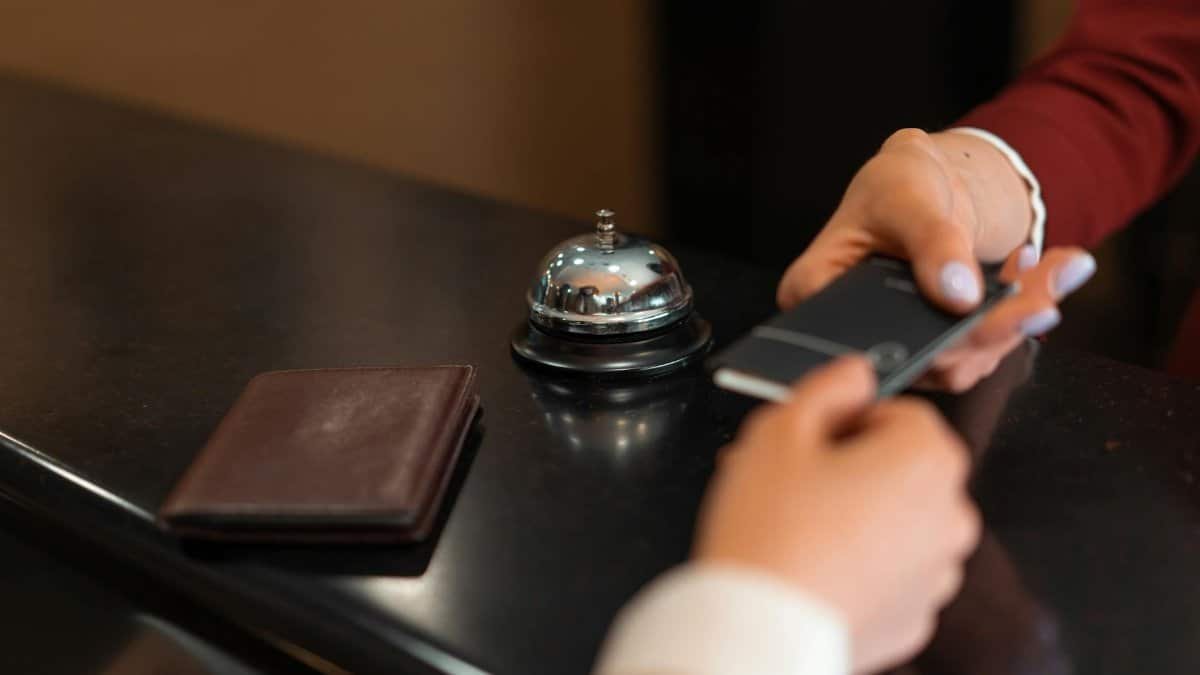 A close-up of a hotel check-in process with a smartphone and card transaction at the reception desk.