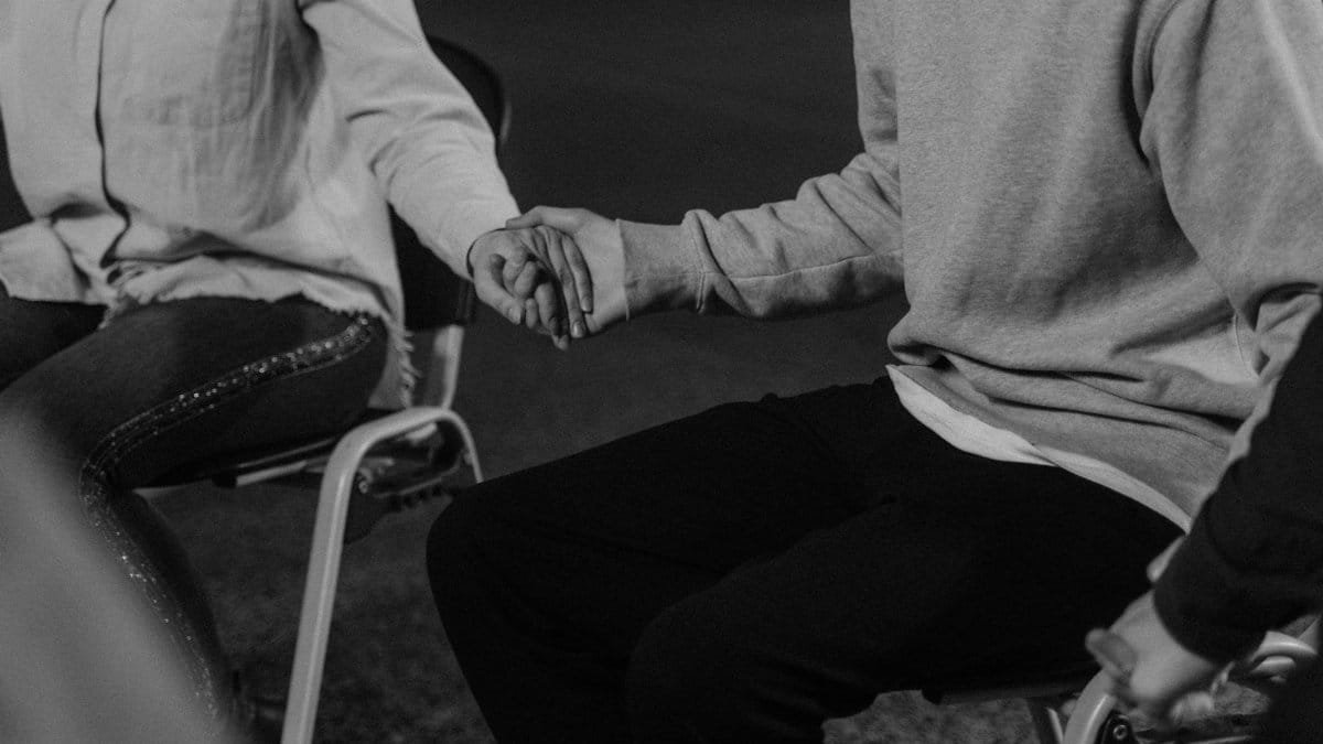 Black and white image of people holding hands in a group therapy session enhancing mutual support.