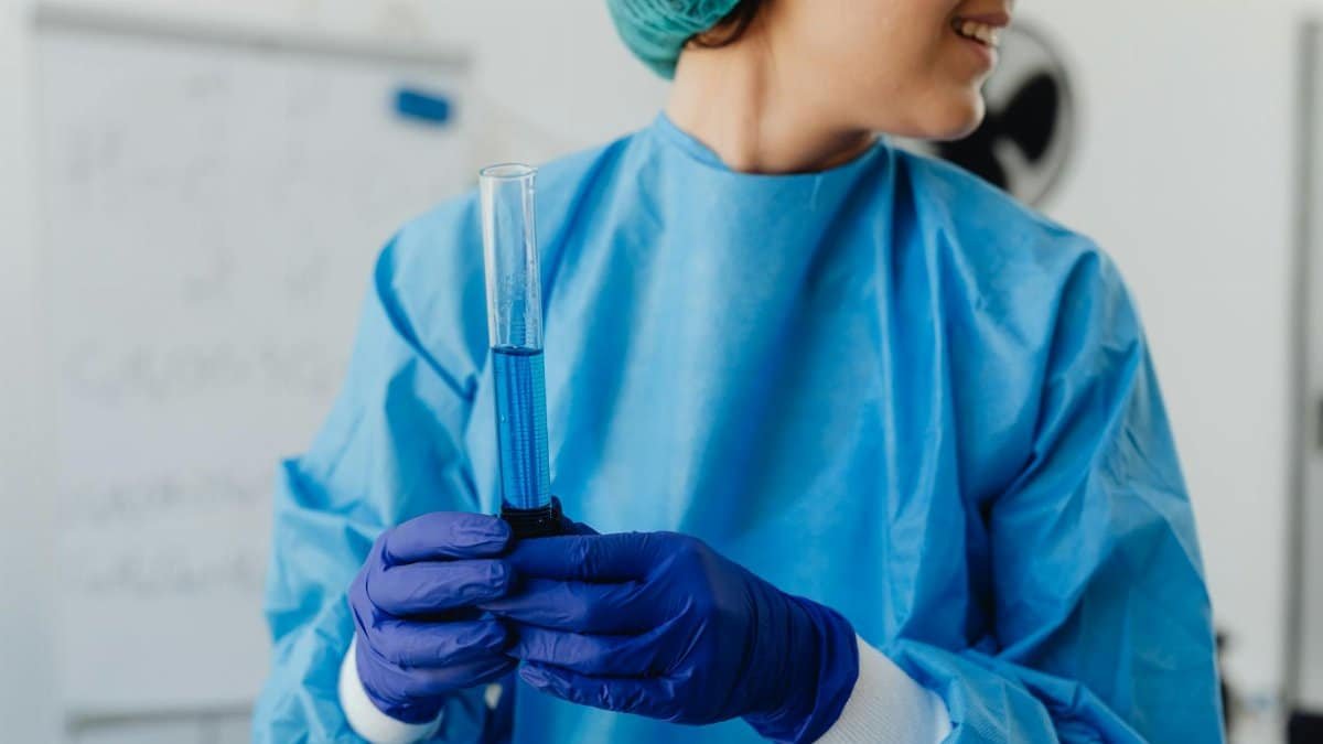 Smiling female scientist holding a blue liquid-filled test tube in a modern lab.