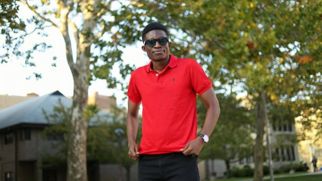 African man wearing sunglasses and red polo shirt standing in a park in Detroit, MI.