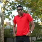 African man wearing sunglasses and red polo shirt standing in a park in Detroit, MI.
