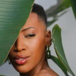 Beautiful portrait of a woman partially hidden behind lush tropical leaves.