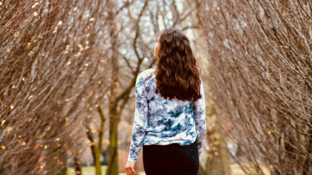 A woman in casual wear walks through a leafless park pathway, capturing the essence of fall.