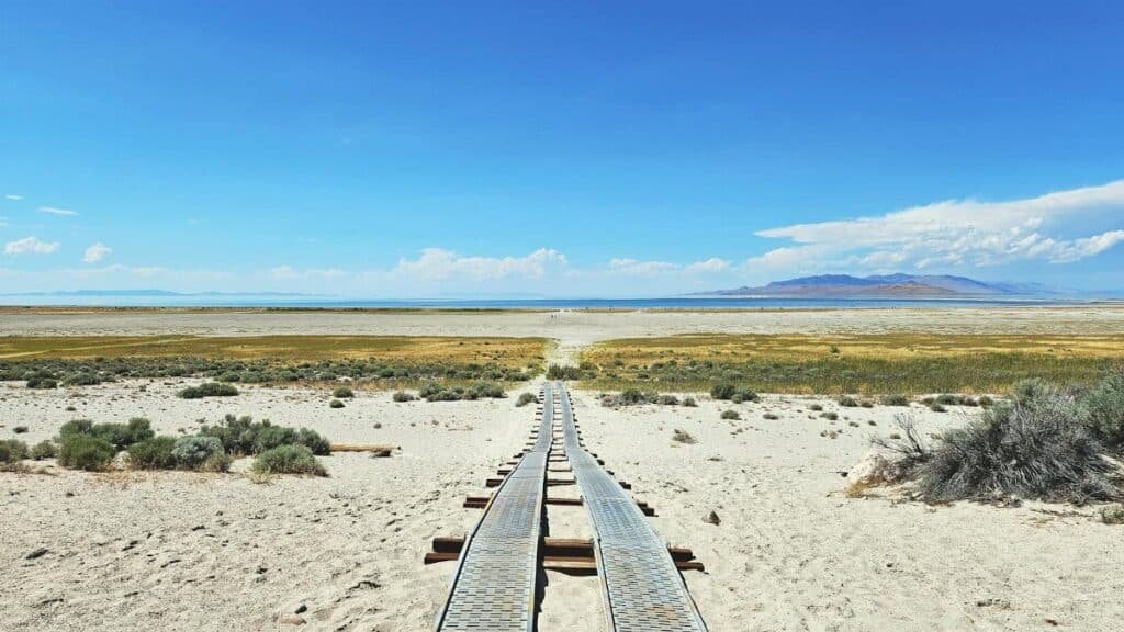 A metal boardwalk stretches across a sandy desert landscape towards the Great Salt Lake in Utah.