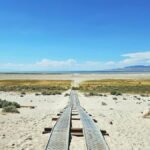 A metal boardwalk stretches across a sandy desert landscape towards the Great Salt Lake in Utah.