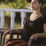 A woman in meditation with eyes closed sitting on a chair outdoors in the sunlight.