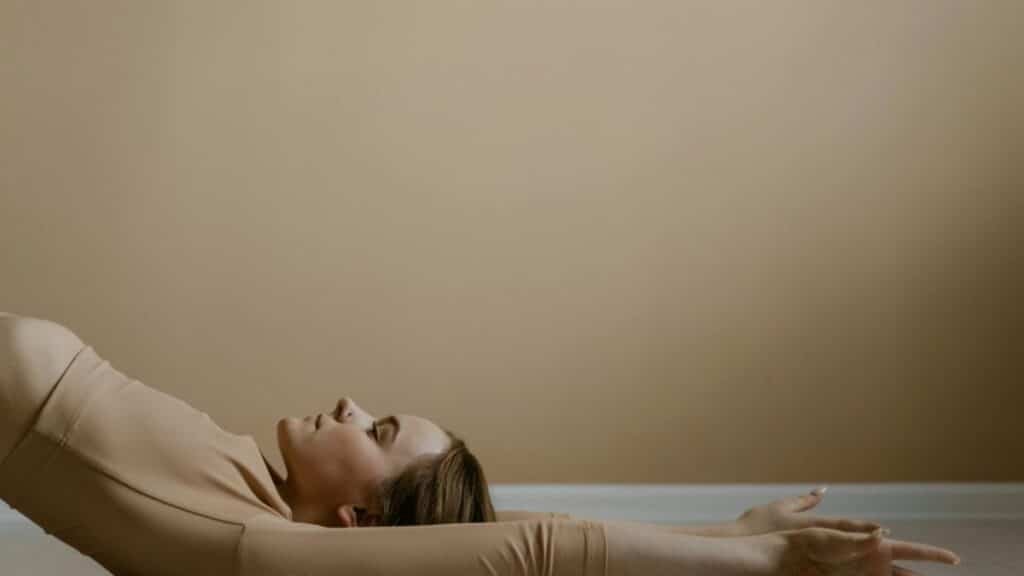 Woman in calm yoga pose, arms extended, in neutral setting.