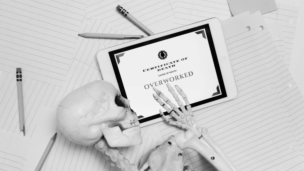 Black and white image of skeleton hand holding tablet with 'Certificate of Death' showing overworked.