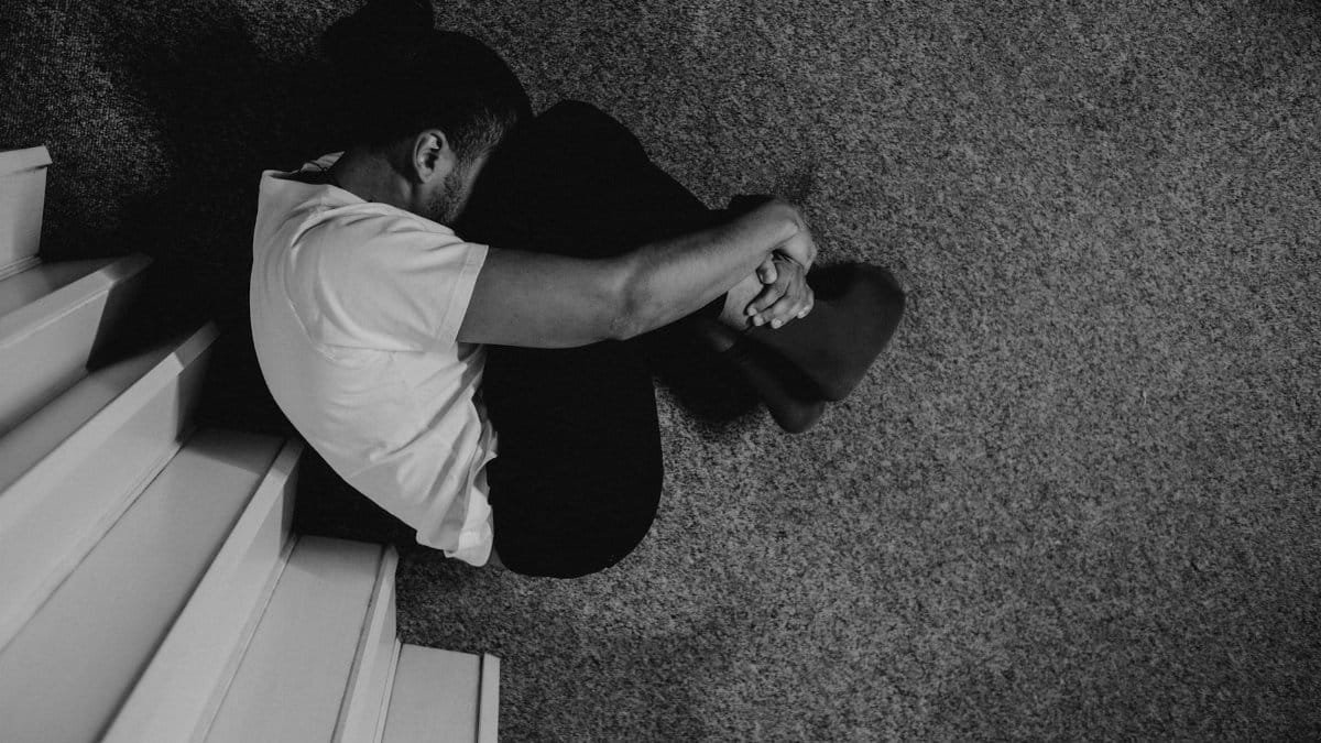 A moody black and white photo of a man sitting on stairs, deep in thought.