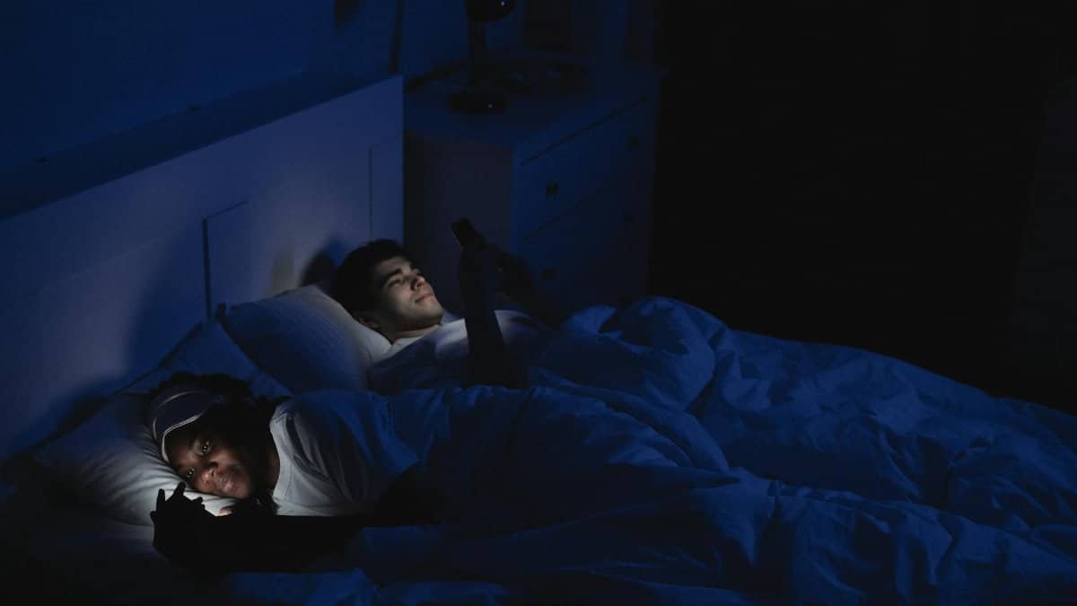 Couple lying in bed at night using gadgets, low light and relaxed mood.