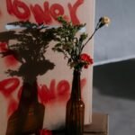 A floral arrangement casts a shadow with 'Flower is Power' sprayed in red, symbolizing peaceful protest.